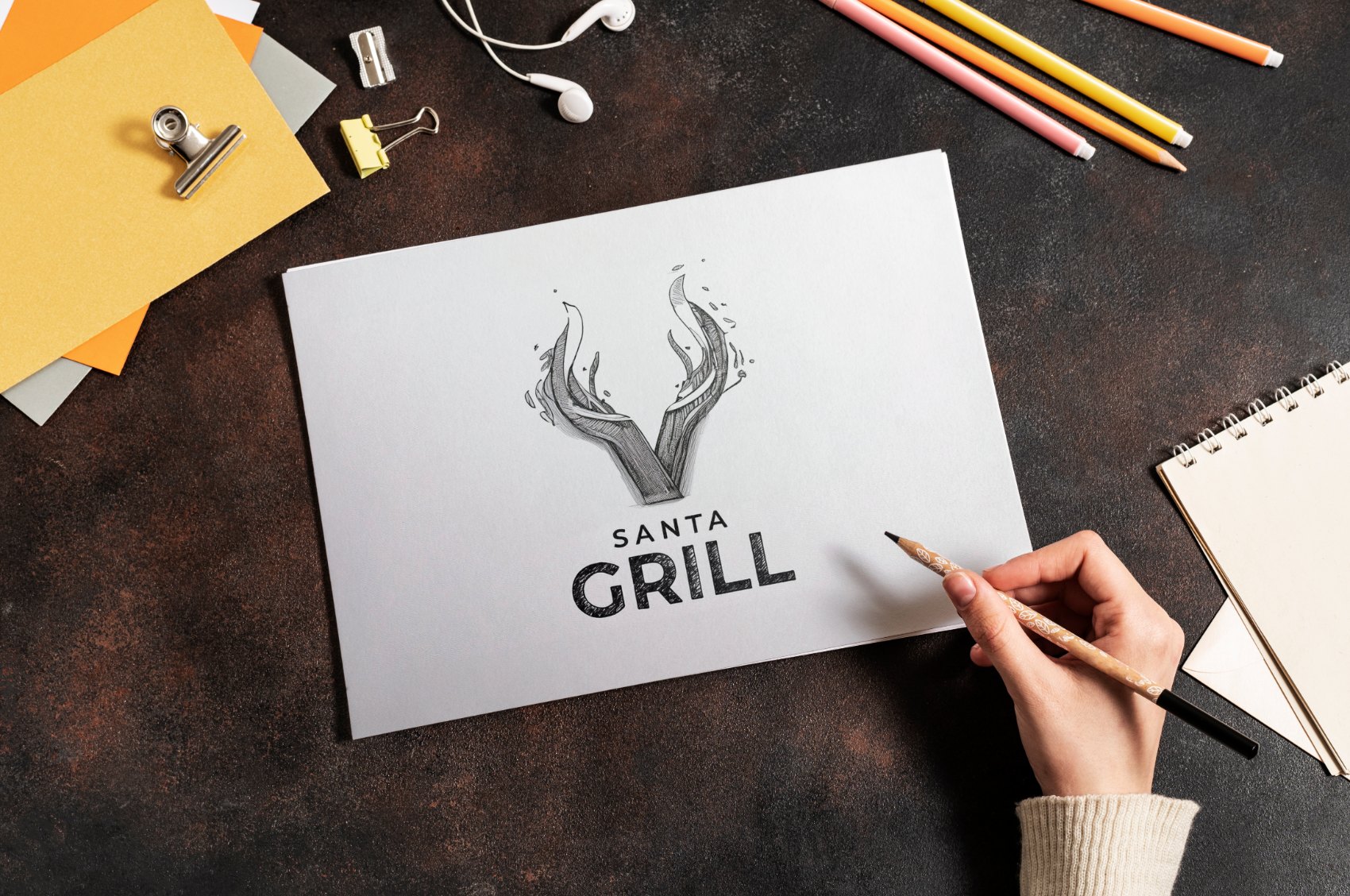 Rascunho a lápis do logotipo Santa Grill sobre a mesa de criação da AMO